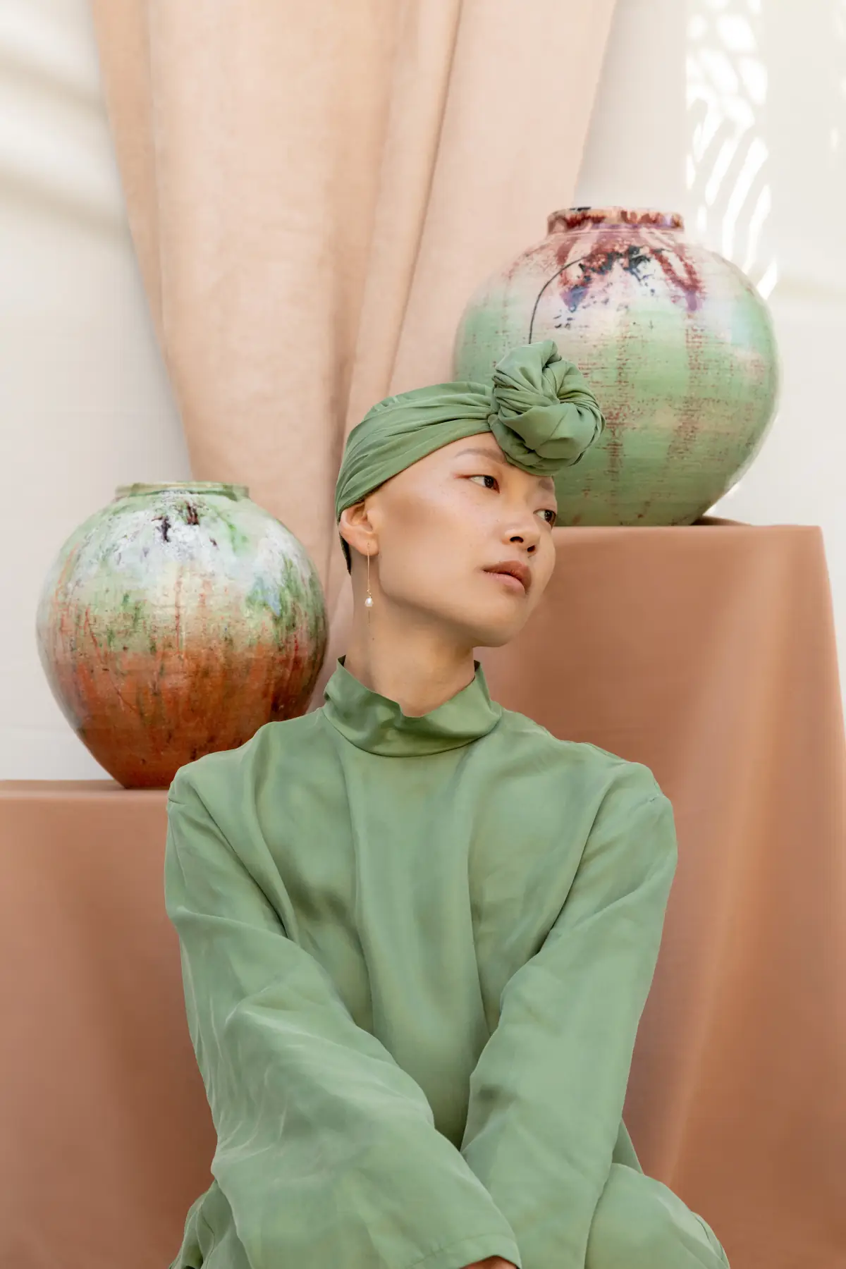 A figure in green silk seated between two large globe vessels in a peach setting