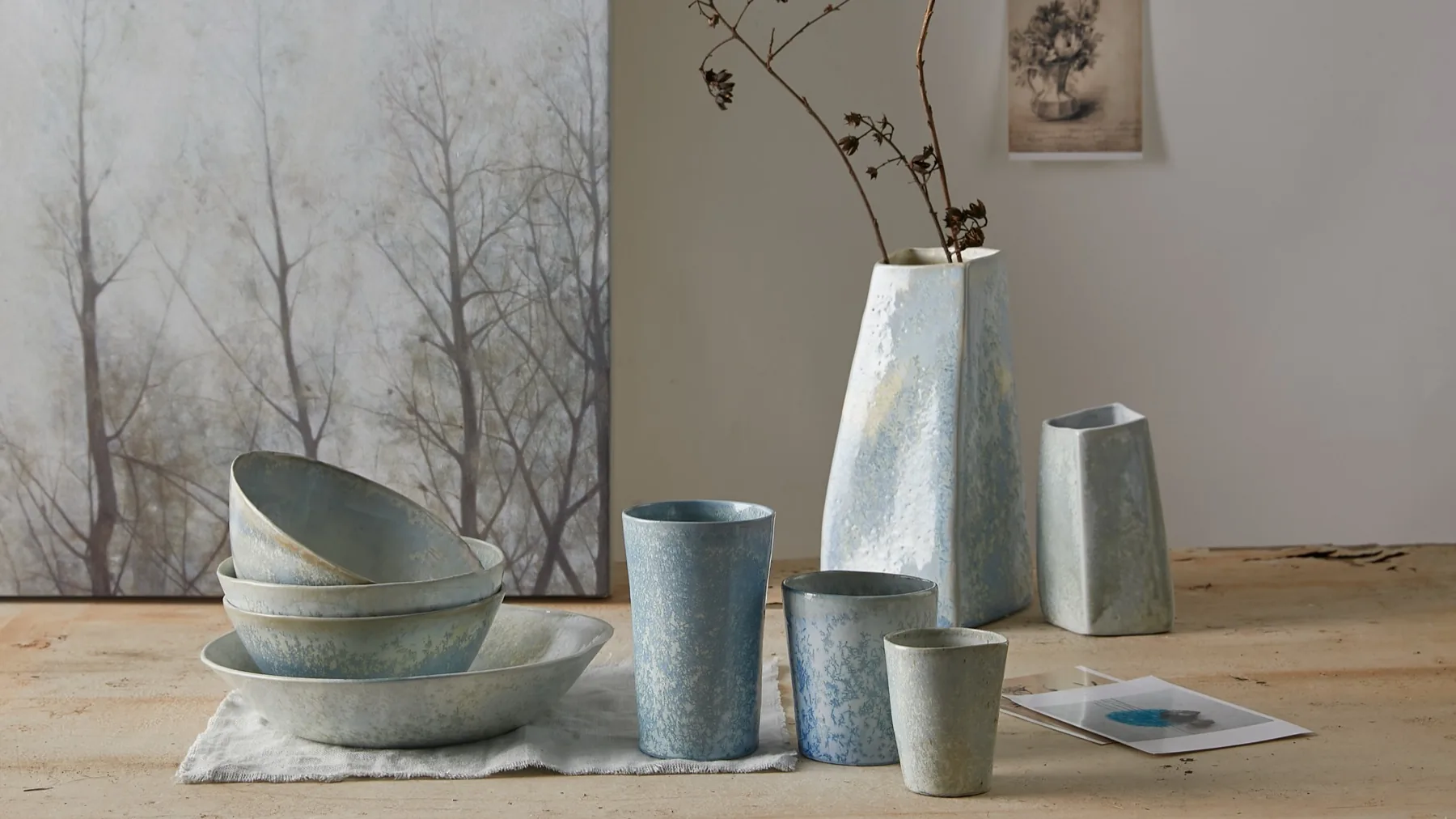 A soft blue ceramic tableware set styled on a wooden table with dried branches