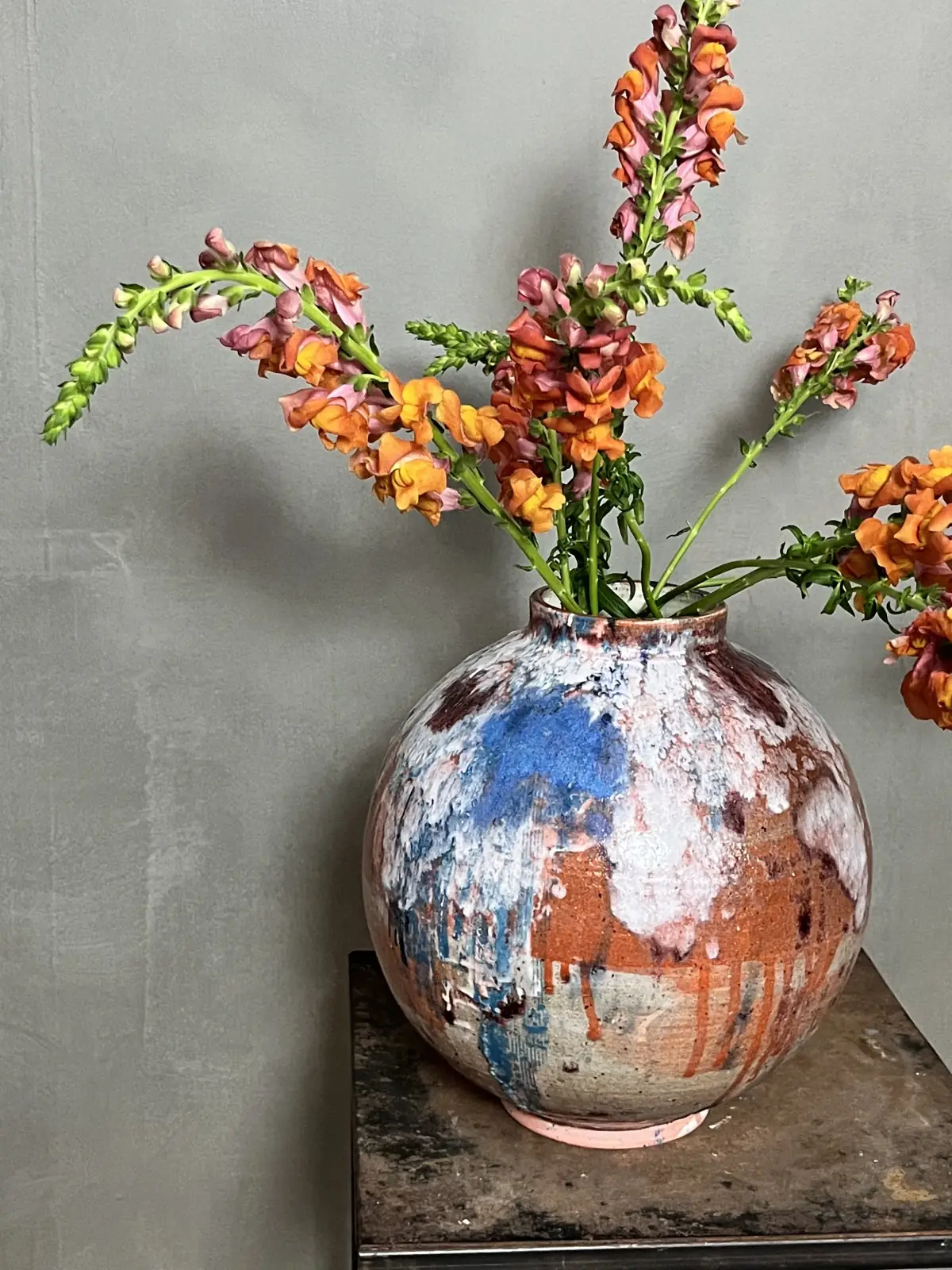 A globular Touches vase with orange snapdragons on an iron side table