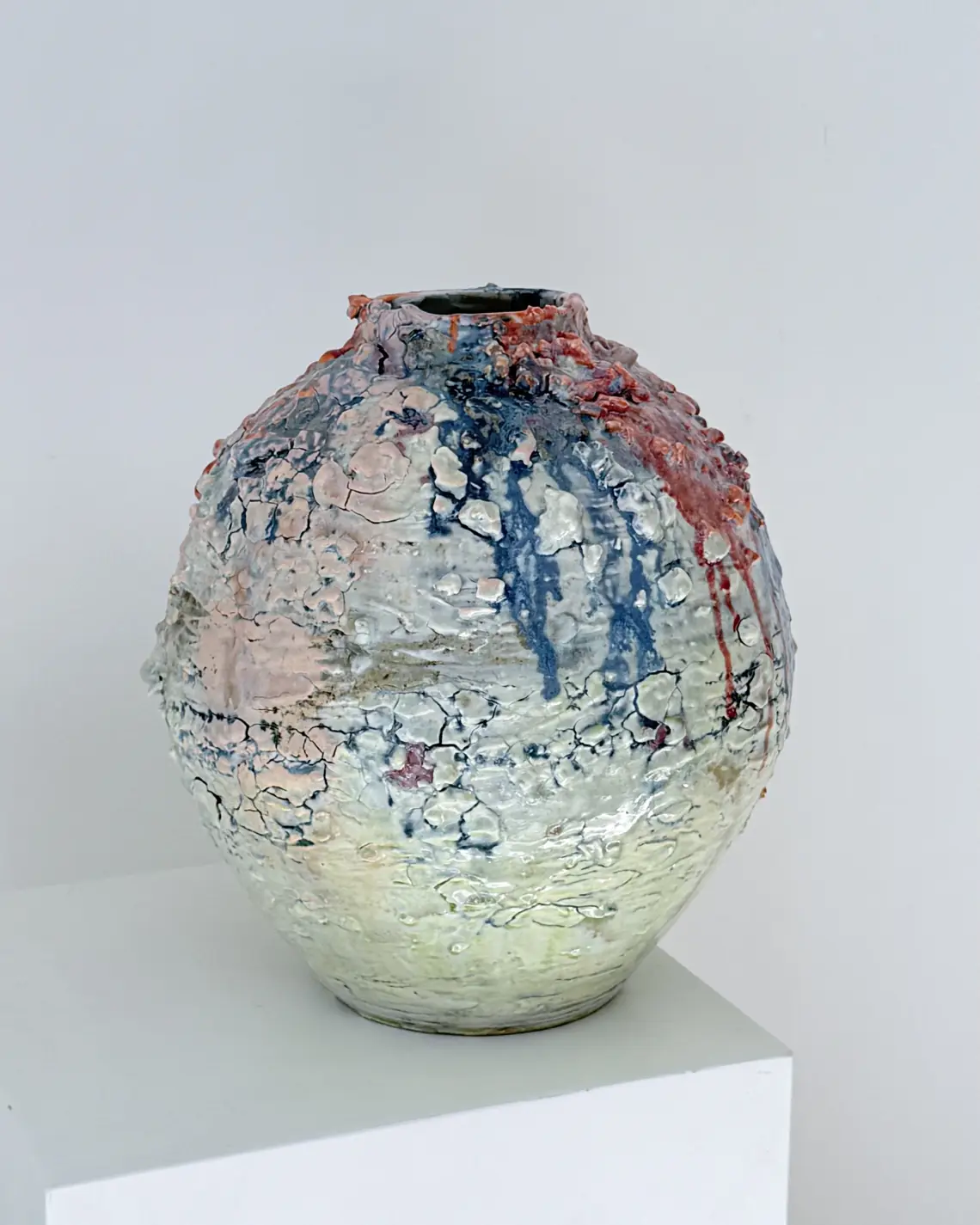 A globular raku vessel with red, blue, and pink crackled glaze on a plinth