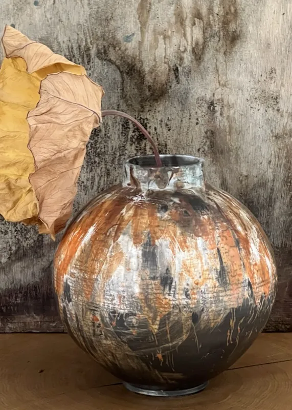 A fallen leaf draped over a glazed copper vessel