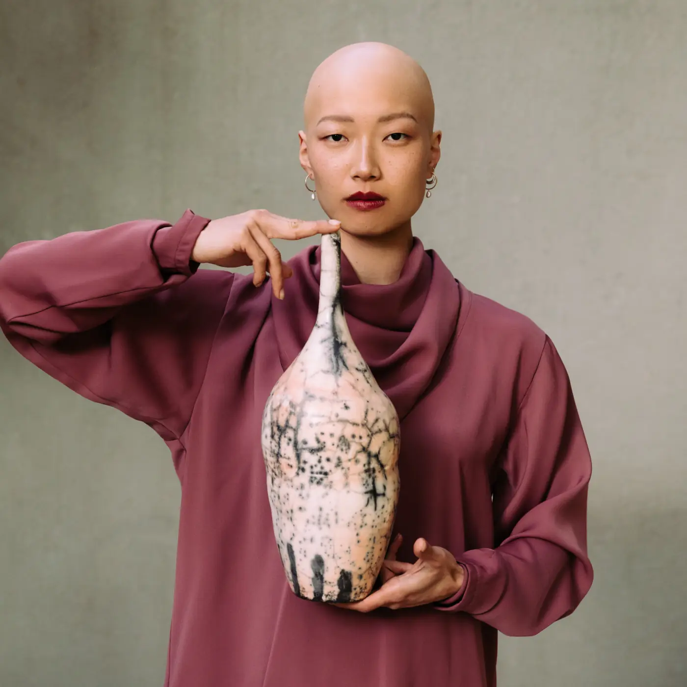 A model in mauve holding a tall narrow raku bottle