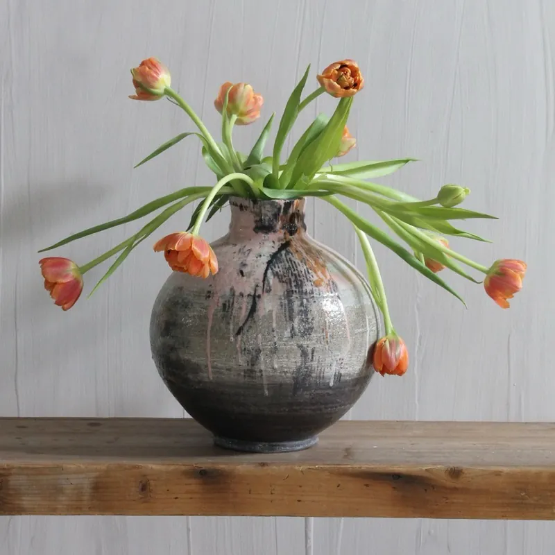 Orange tulips spilling from a black-glazed vase