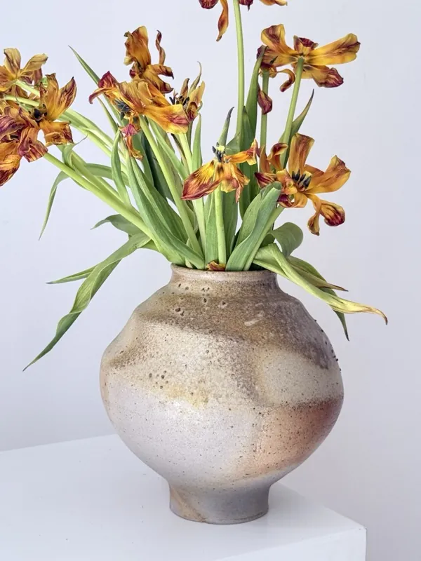 Wilted orange tulips in a sandy stoneware vase