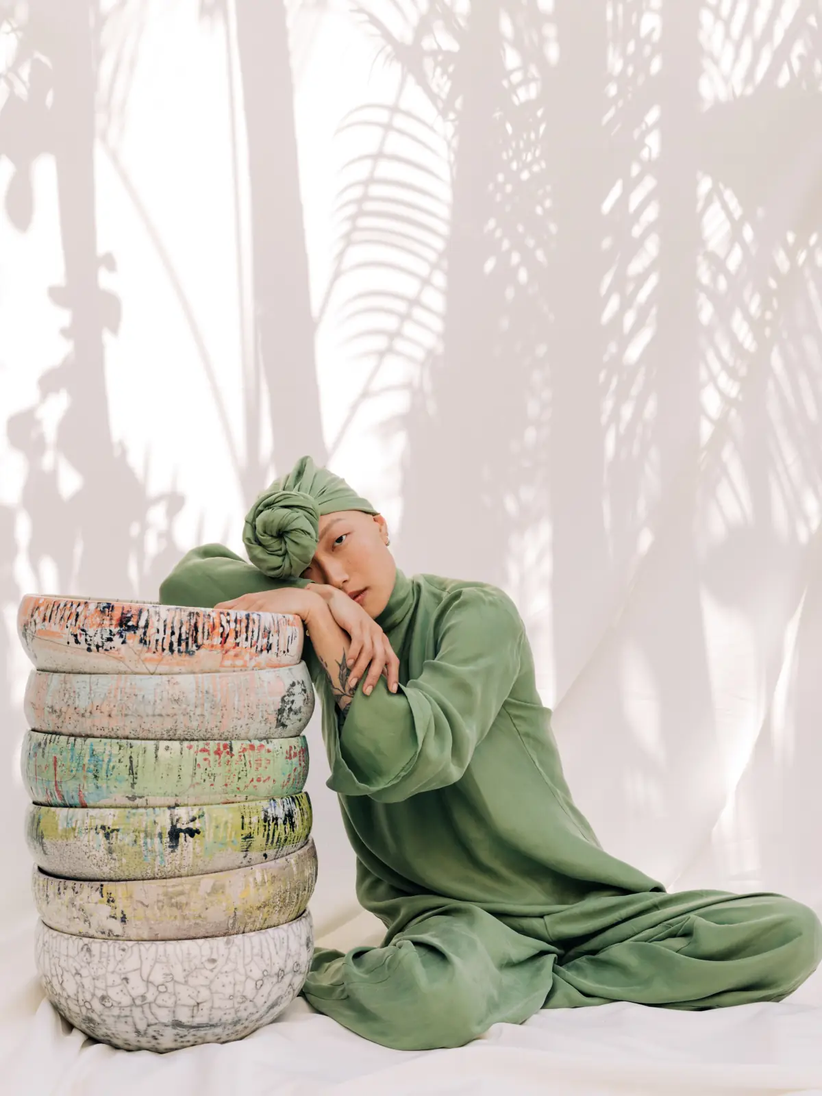 A model in green silk resting on a stack of raku bowls